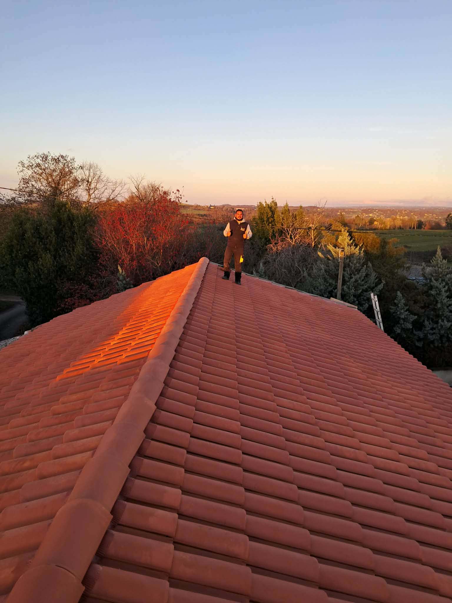 Couvreur debout sur toiture tuiles canal terminée — coucher de soleil